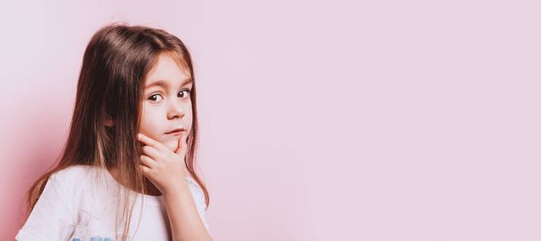 Funny portrait of little doubt girl on pink background. - Foto, imagen