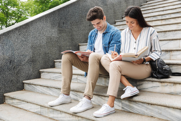 Amazing loving couple students colleagues outdoors outside on steps reading book writing notes studying. - Valokuva, kuva