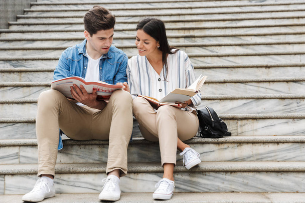 Amazing loving couple students colleagues outdoors outside on steps reading book writing notes studying. - Valokuva, kuva