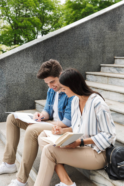 Amazing loving couple students colleagues outdoors outside on steps reading book writing notes studying. - Fotoğraf, Görsel