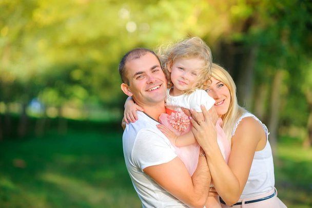 glückliche Familie im Abendpark, eine Tochter im Arm und lächelnd - Foto, Bild