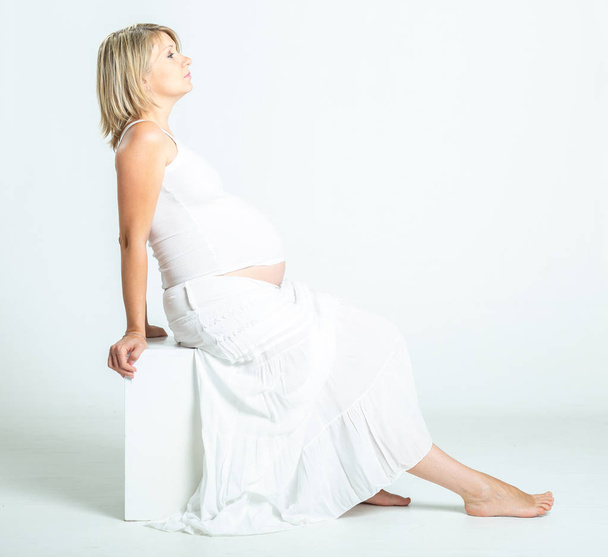 Terhes nő fehér felső és szoknya pózol stúdióban - Fotó, kép