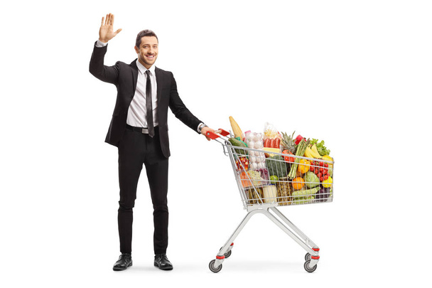 Businessman with a shopping cart full of food products waving at - Foto, imagen
