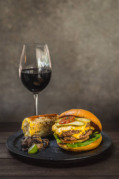 All-American burger.  A double wagyu fat and chuck blend patty and bacon ketchup in a brioche bun.  Served with Mexican corn and sauteed thyme mushrooms. - Photo, Image