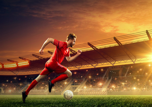 Piłka nożna gracz biegnie z piłką. Oświetlone nocne boisko do piłki nożnej z dramatycznym nocnym niebie - Zdjęcie, obraz