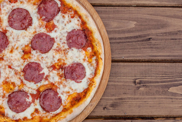 Italian Pepperoni pizza with salami on dark wooden background top view. Italian traditional food. Popular street food - Фото, изображение