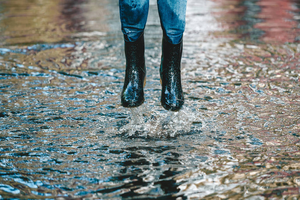 Legs of woman in shabby jeans and in rubber boots jump in big puddle - Foto, Imagen