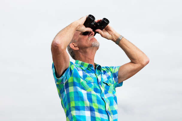 Senior man with beard and glasses using binoculars outdoors in g - Fotoğraf, Görsel