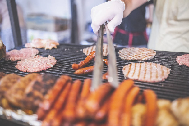 Man preparing burgers and sausages at street festival. - Фото, изображение