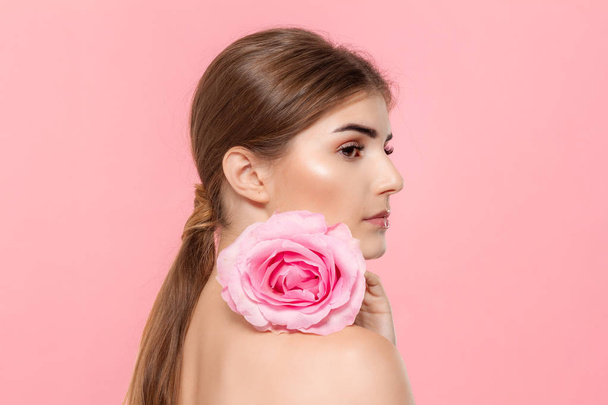 Close-up portrait of a beautiful young girl with pink rose flower isolated over pink background. - Photo, Image