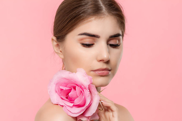 ピンクの背景の上に孤立したピンクのバラの花を持つ美しい若い女の子のクローズアップ肖像画. - 写真・画像