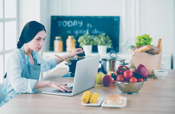 Young Woman in kitchen with laptop computer looking recipes, smiling. Food blogger concept - Photo, image