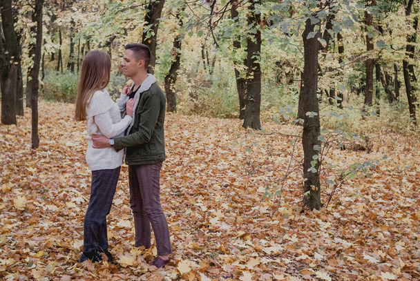 Para w miłości stoją jesienią opadłych liści w parku, ciesząc się pięknym jesiennym dniem. Człowiek uściski dziewczynę - Zdjęcie, obraz