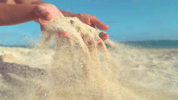 SLOW MOTION, FECHAR-se: suave brisa de verão varre a areia das mãos suaves da menina brincalhão. Fotografia cinematográfica de pequenos grãos de areia voando através da praia ensolarada remota em belas Ilhas Cook
. - Filmagem, Vídeo