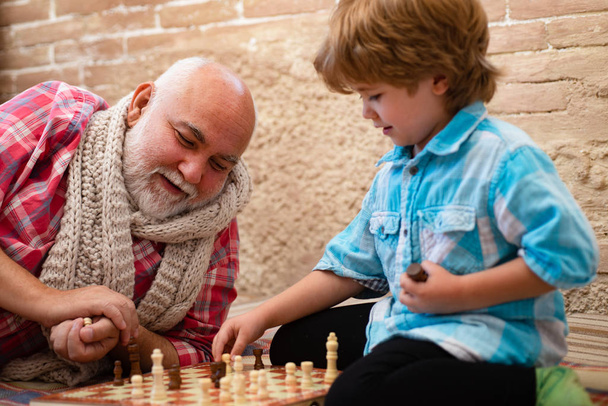 Um rapazinho a jogar xadrez com o avô. Xadrez. Miúdo a jogar xadrez. Avô e neto estão jogando xadrez e sorrindo enquanto passam o tempo juntos em casa
. - Foto, Imagem