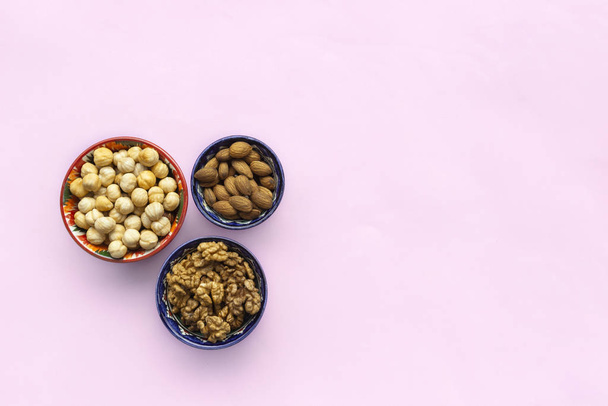 Assortment  mix of nuts, hazelnuts, almonds, walnuts in bowls on pink background. Flat lay, top view, copy space - Zdjęcie, obraz