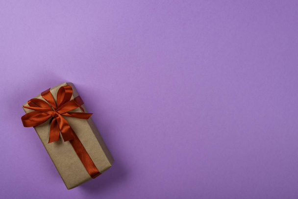 Подарочная коробка с бантом на фиолетовом неоновом фоне. Пространство для текста в правой части изображения
. - Фото, изображение