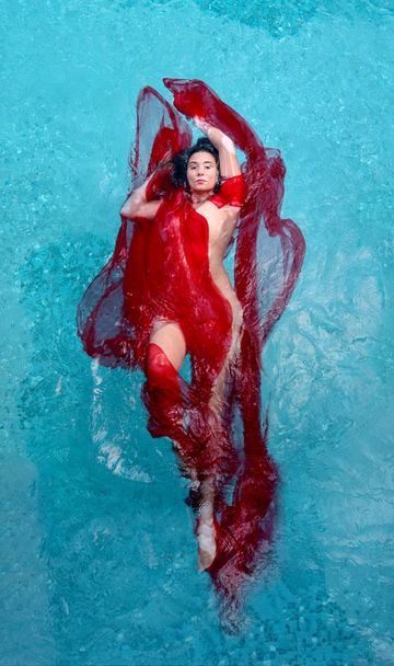 beautiful young woman with vitiligo disease in red evening dress, floating weightlessly elegant in the pool - Photo, Image