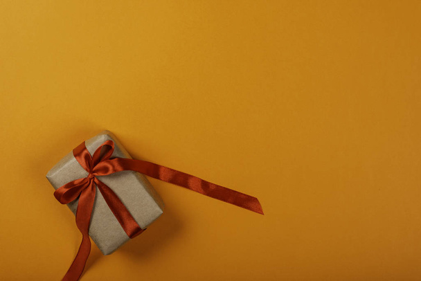 Gift box with bow over orange background. Space for text on the right side of the image. - Photo, image