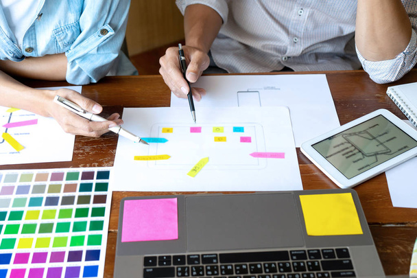 Groep jonge ontwerpers werkt in het kantoor aan het ontwerpen van een nieuw product, gebruik kleurenkaart en computer laptop voor nieuwe smartphone design concept - Foto, afbeelding