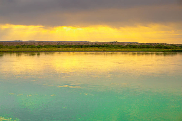 Ποτάμι με το ηλιοβασίλεμα. Η αντίθεση του ουρανού πάνω από το ποτάμι. Χρυσές ακτίνες του ήλιου το ηλιοβασίλεμα. Καθαρός γαλάζιος ποταμός. Καλοκαίρι στο Καζακστάν. - Φωτογραφία, εικόνα