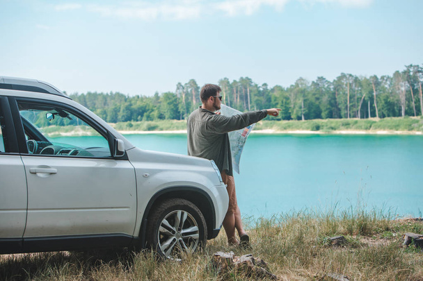 車の旅行のコンセプトの男は、背景にSUV車のフード湖で男を見て - 写真・画像