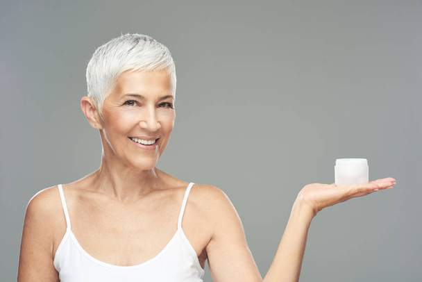 Gorgeous smiling Caucasian senior woman trying out new anti age cream and looking at camera. Beauty photography. - Photo, Image
