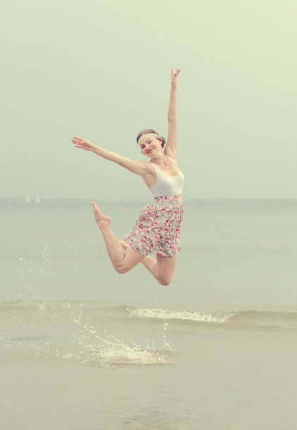 Young happy woman jumping on a sea shore - 写真・画像