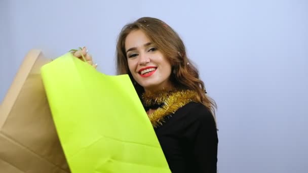 Young woman in black dress, holding colorful shopping bags and smiling isolated on white background in black friday holiday, Christmas or New Year time. Slow motion. - Video