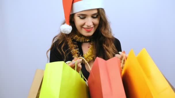 Young woman in black dress and red Santa Claus hat showing colorful shopping bags and smiling isolated on white background. Black friday, Christmas or New Year concept. Slow motion. - Video, Çekim