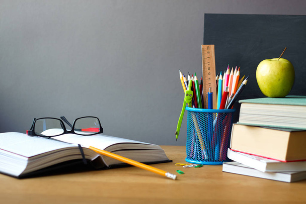 School supplies, stack of books, chalk board and open book with glasses on a wooden surface, selective focus - Photo, Image