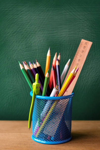 Recipiente de metal azul com material escolar em um pano de fundo de um quadro verde com manchas de giz, foco seletivo, espaço de cópia
 - Foto, Imagem