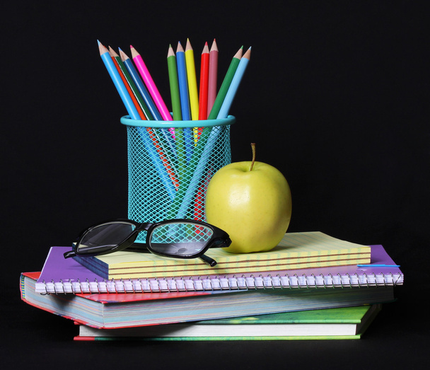 Torniamo al concetto di scuola. Una mela, matite colorate e bicchieri su mucchio di libri su sfondo nero
. - Foto, immagini