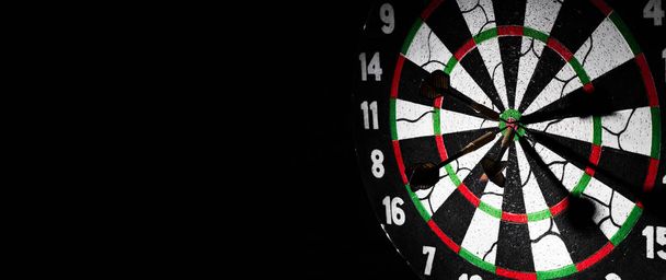 Dartboard with dart arrow hitting the center on a dark black background with copy space. - Foto, afbeelding