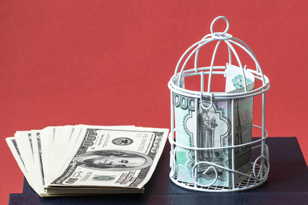 el rublo cerrado en una jaula apretada y un paquete de dólares al lado del libro, el fondo es rojo
 - Foto, imagen
