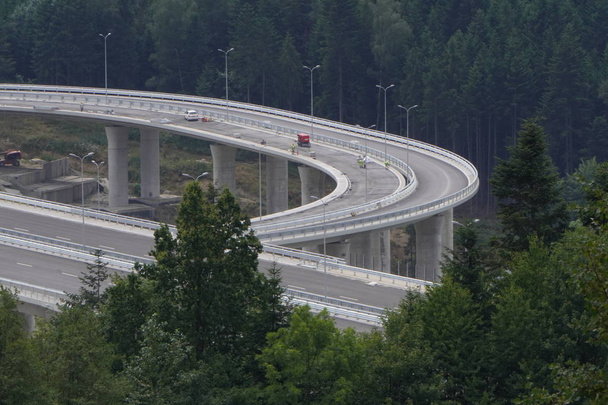 Bau einer modernen Überführung in den Bergen, Hochgeschwindigkeits-Betonstraße in einer bergigen Gegend, viele hohe Bäume an den Hängen - Foto, Bild