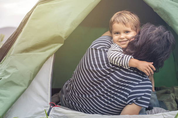 Isänpäivä. Onnellinen perhe lomalla telttailemassa teltassa. Iloinen isä ja poika matkustavat yhdessä luonnossa, pystyttivät teltan telttailuun. Isä ja poika hauskaa raitista ilmaa, auringonlaskun aikaan
 - Valokuva, kuva