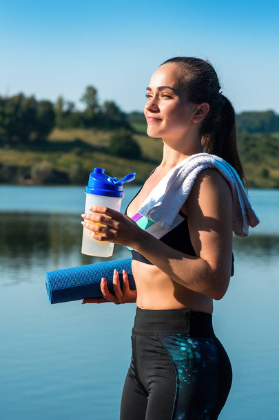 Beautiful girl drinks water during a sports training on a background of beautiful nature - Photo, Image
