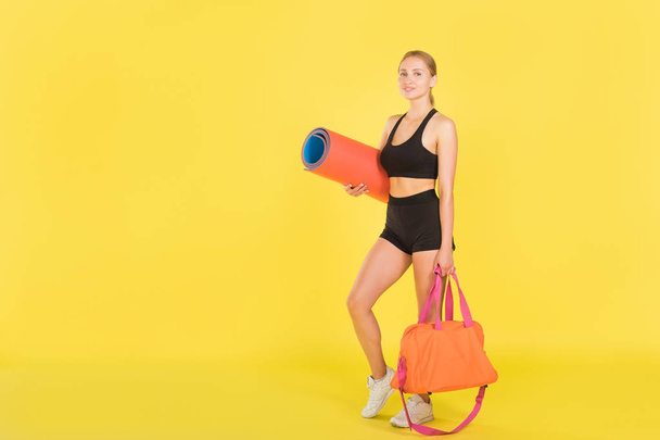 Woman with a sports bag and yoga mat on a yellow background. Woman athlete. - Фото, зображення