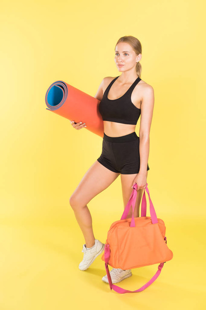 Woman with a sports bag and yoga mat on a yellow background. Woman athlete. - Photo, Image