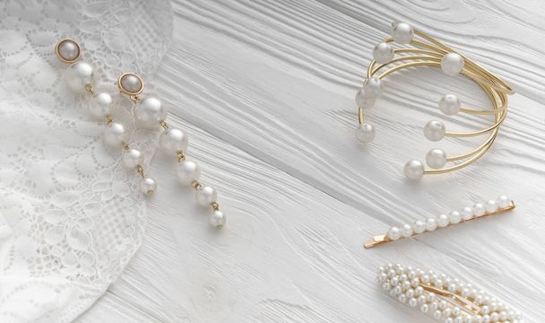 Top view of golden bracelet and earrings and hair pins with pearls jewelry on white wooden background - Photo, Image