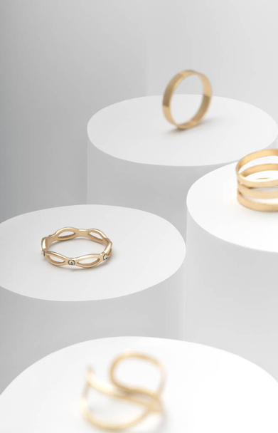Modern Golden rings set on white cylinders top view - Фото, изображение