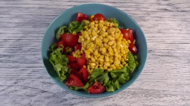 Ensalada de verduras con tomates, hierbas y maíz en un plato de color aguamarina. Sobre una mesa blanca pintada de madera
 - Metraje, vídeo