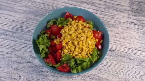 Vegetable salad with tomatoes, herbs and corn in a plate of aquamarine color. On a wooden painted white table - Footage, Video