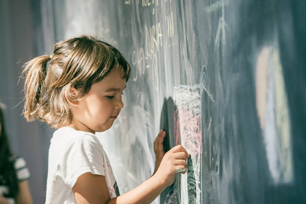 Beautiful little girl drawing on a blackboard at playground - Foto, imagen