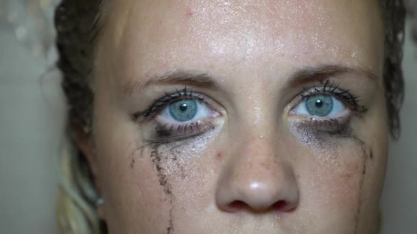 Smeared mascara on female eyes. A wet girl is looking into the frame. Flowed mascara on the blue eyes of the girl. Wet girl with leaking mascara in front of her eyes. Face close up - Footage, Video