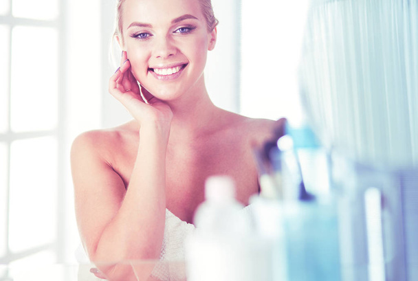 Young woman in bathrobe looking in bathroom mirror - Foto, Imagen