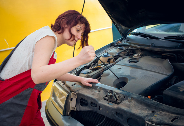 Kobieta mechanik w czerwonym pracy nosić kombinezon w samochodzie mechanik sklep sprawdzanie oleju samochodowego. - Zdjęcie, obraz