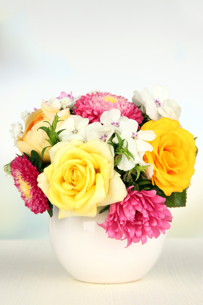 Beautiful bouquet of bright flowers in color vase, on wooden table, on bright background - Foto, Bild