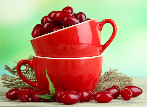 Fresh cornel berries in red cups on wooden table - Foto, imagen